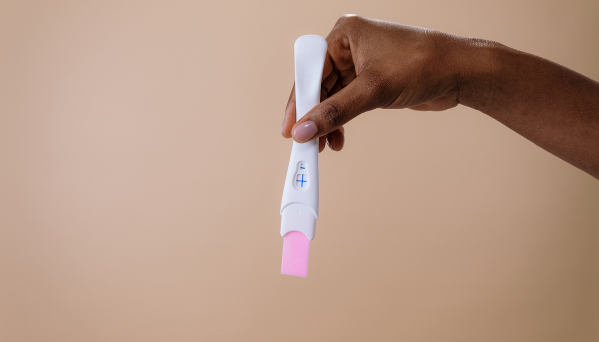 A hand holds a positive pregnancy test with a blue plus sign, symbolizing the question many women ask when their period is late. While pregnancy is one reason, stress, weight changes, illness, or thyroid issues can also cause missed periods.