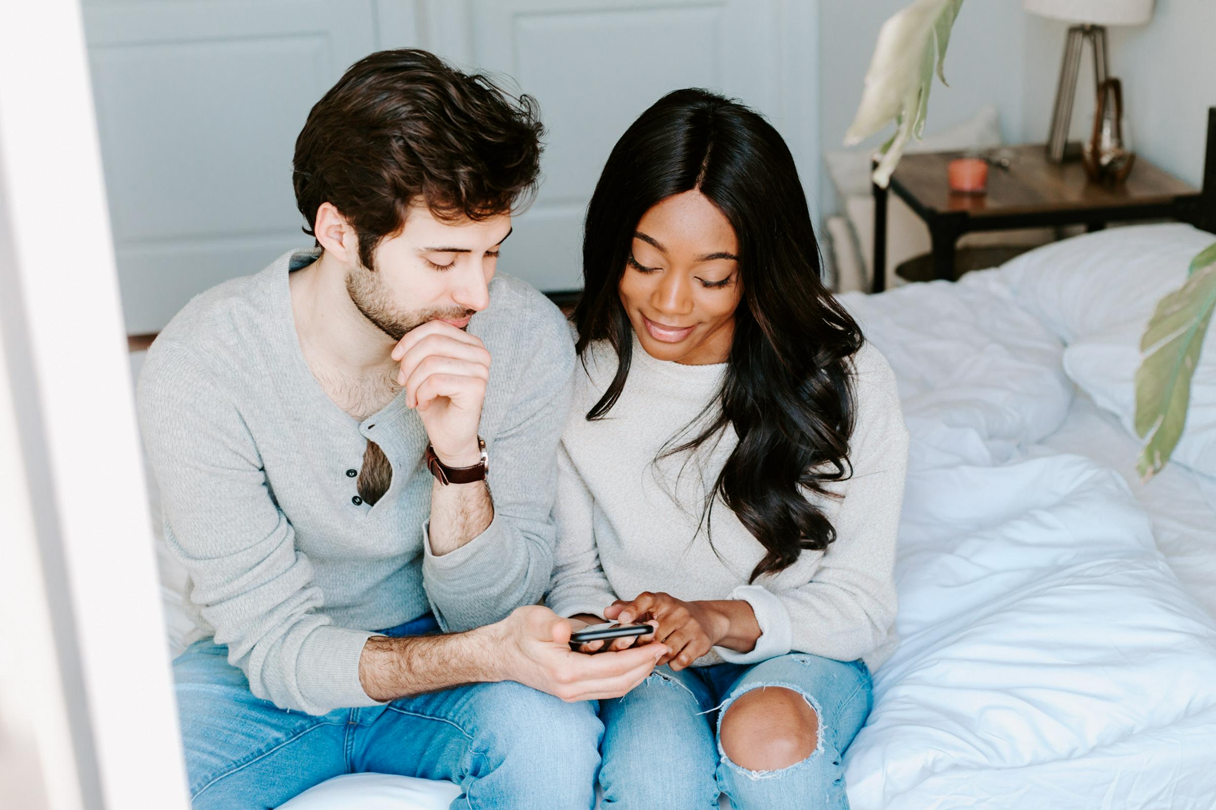 Couple sitting together on a bed, looking at a smartphone while reviewing cycle data.